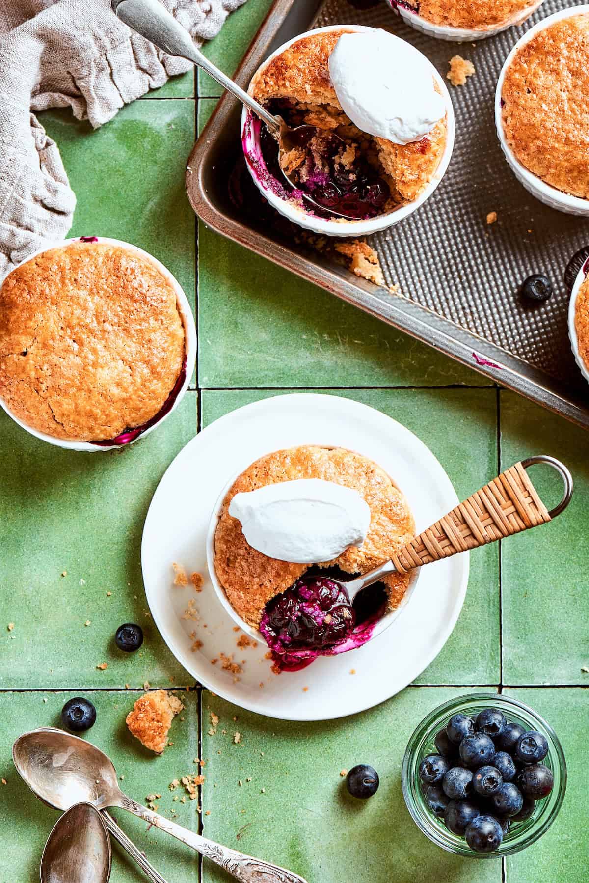 Mini blueberry cobblers on sheet pan, countertop, and plate.