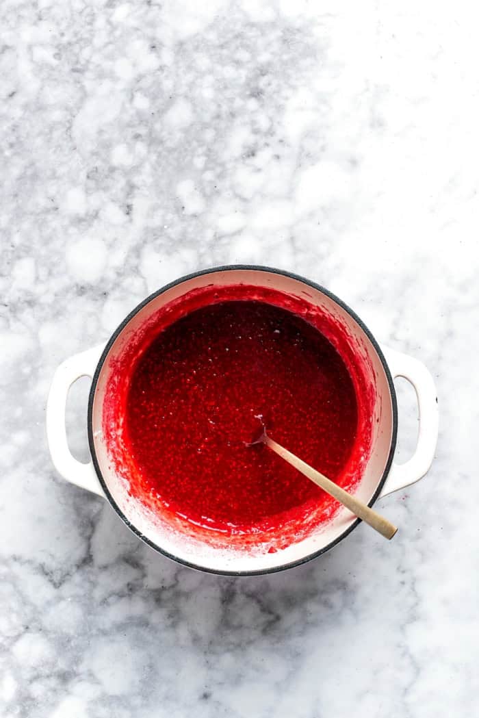 This rich raspberry cheesecake is sure to make your all-time-favorites list. It's rich, creamy, and elegant, but surprisingly easy to make! Overhead view of raspberry sauce in pan with spoon