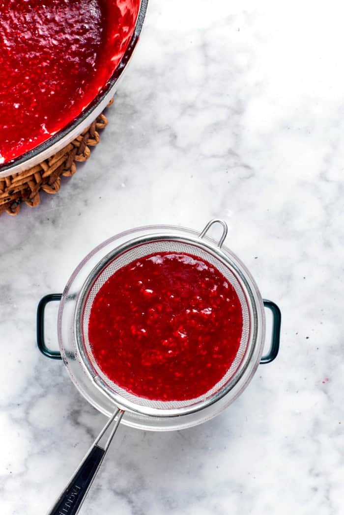 This rich raspberry cheesecake is sure to make your all-time-favorites list. It's rich, creamy, and elegant, but surprisingly easy to make! Overhead view of raspberry sauce being strained into bowl