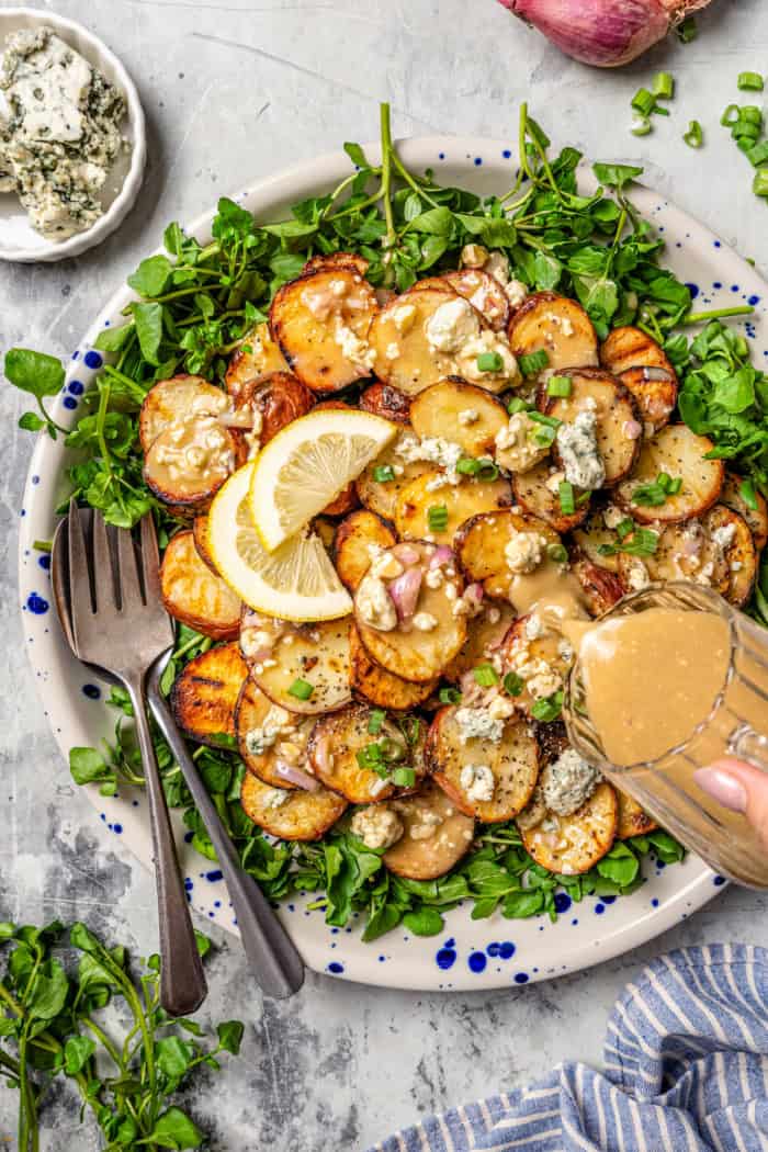 Pouring blue cheese vinaigrette onto platter of grilled potato salad