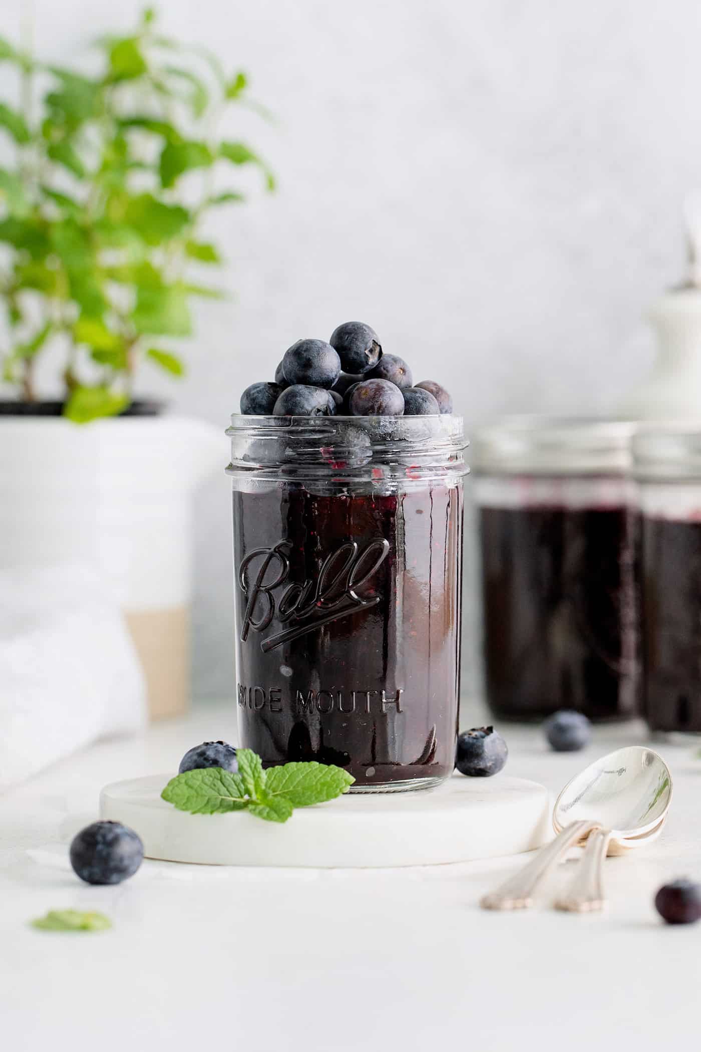 Made with just 4 ingredients, this Homemade Blueberry Jam with Mint is dark and fruity, with a sweet but cool and refreshing flavor. A jar of blueberry jam with more blueberries on top