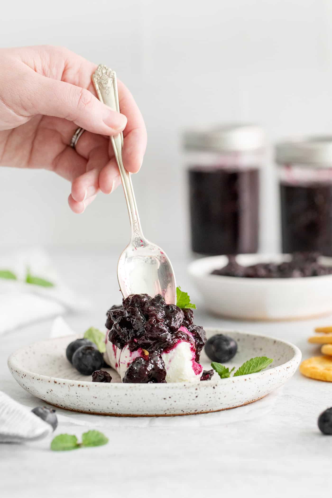 A hand spooning blueberry jam over ice cream