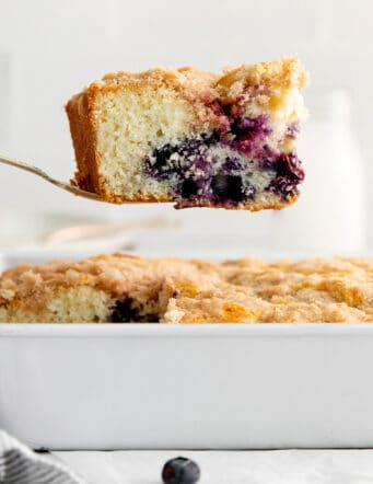 A spatula lifting a slice of blueberry tea cake out of the baking dish