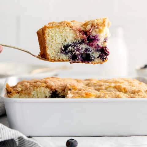 A spatula lifting a slice of blueberry tea cake out of the baking dish