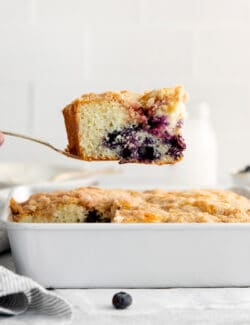 A spatula lifting a slice of blueberry tea cake out of the baking dish