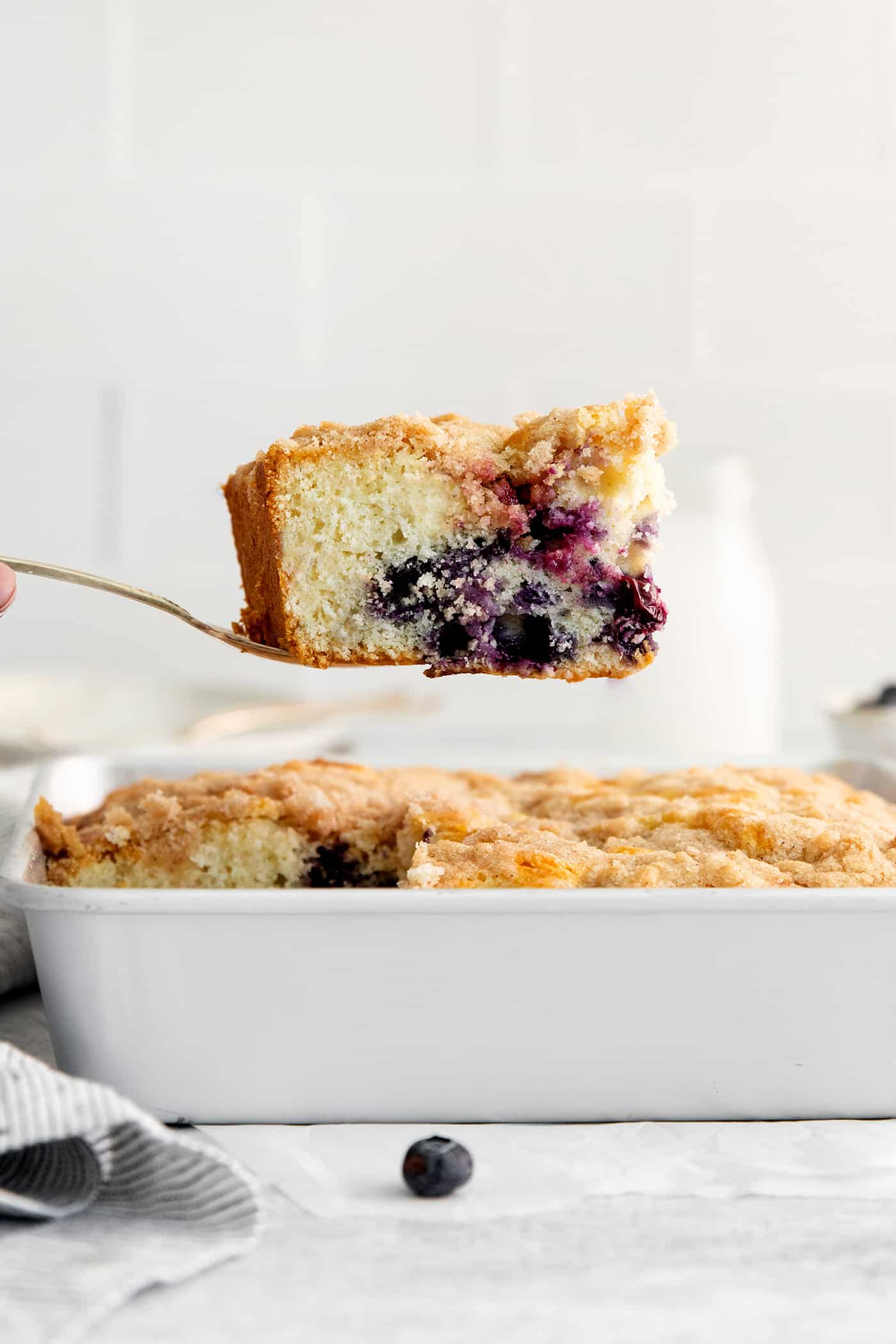 A spatula lifting a slice of blueberry tea cake out of the baking dish