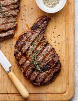 Grilled ribeye steak on cutting board with sprig of thyme.