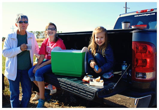 Two Girls Sitting on the Back of a Truck With Their Grandma