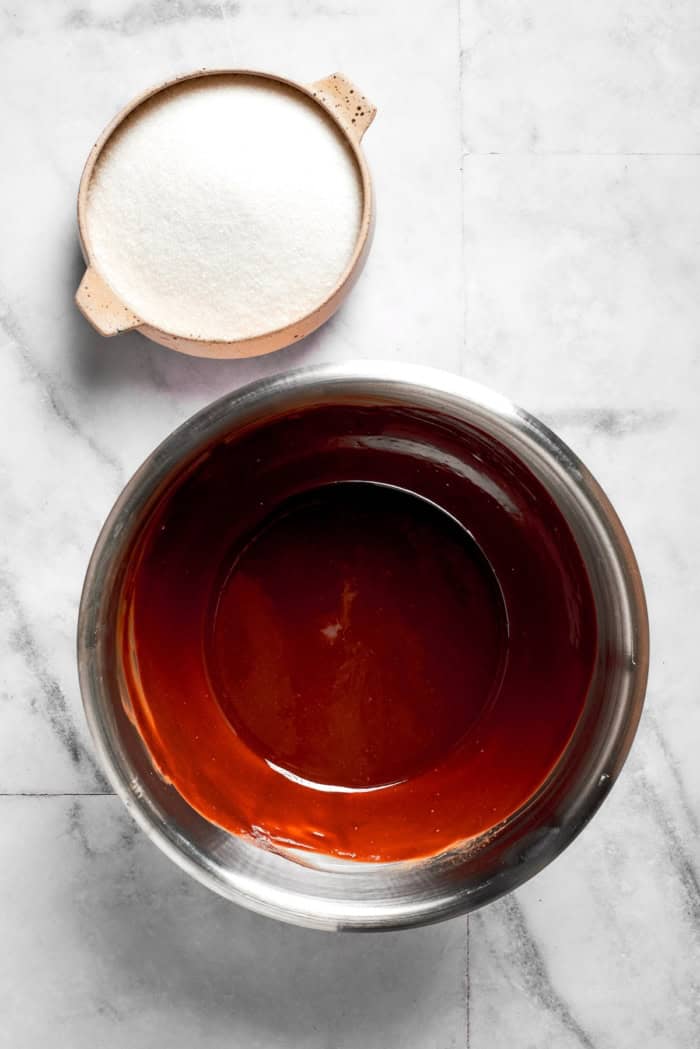 Overhead view of sugar in bowl with bowl of melted butter and chocolate