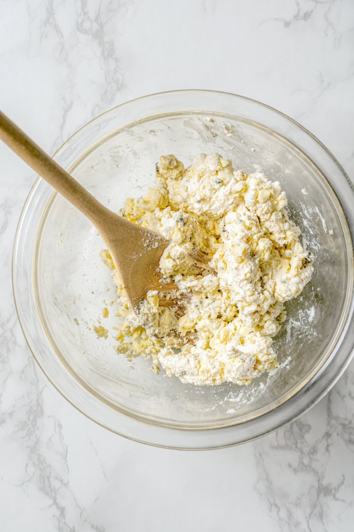 Stirring together blue cheese and cream cheese in glass bowl