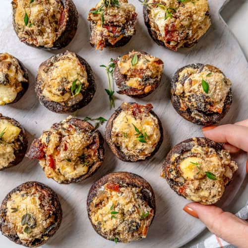 Hand pulling stuffed mushroom from serving board