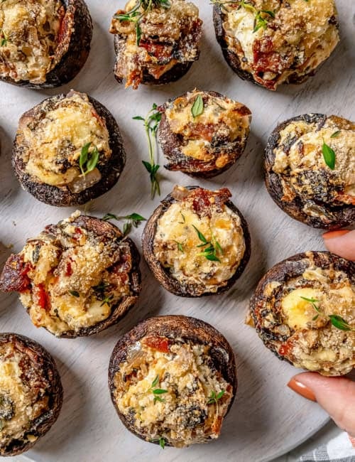 Hand pulling stuffed mushroom from serving board