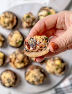 Hand holding sliced stuffed mushroom with bacon and blue cheese to show interior