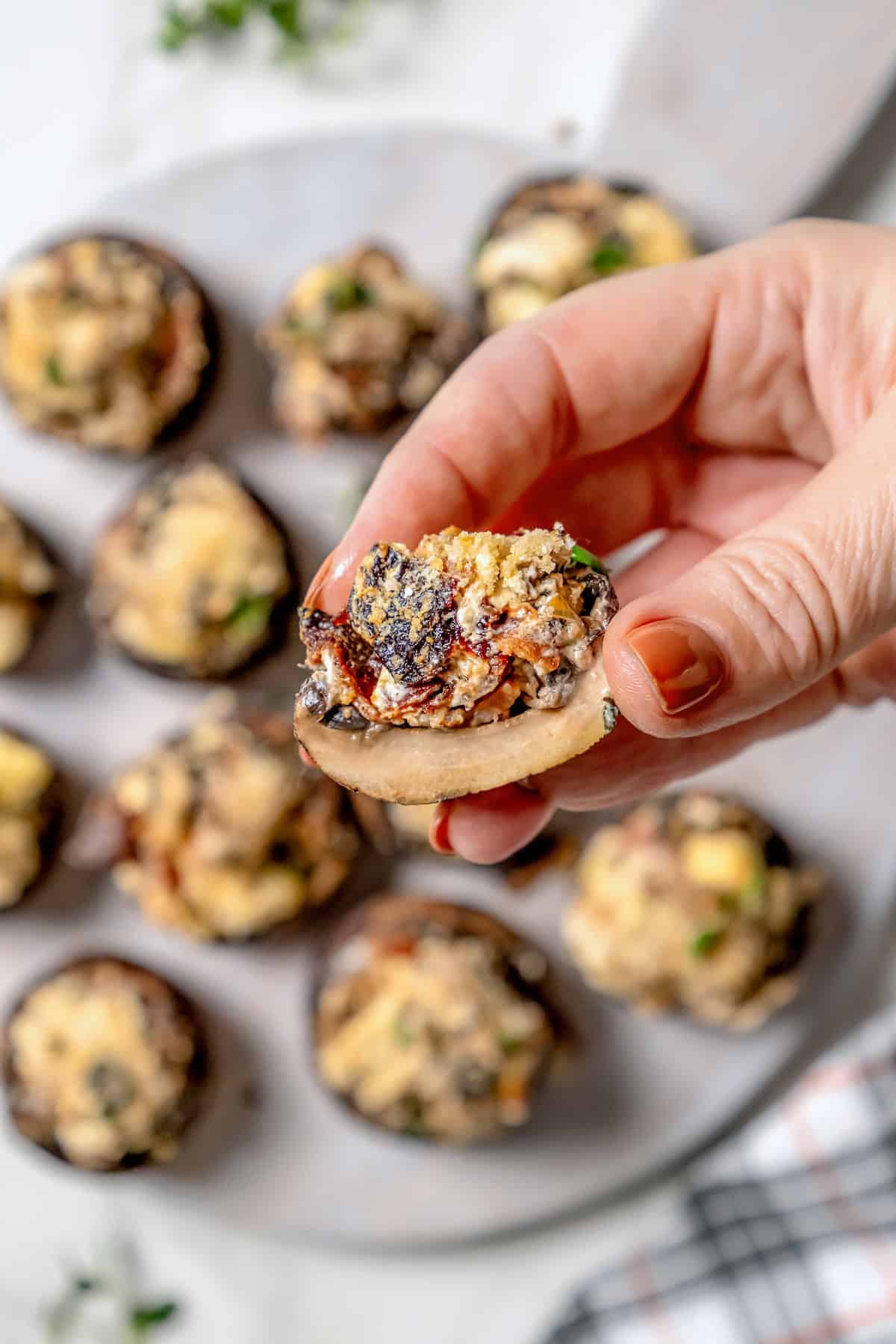 Hand holding sliced stuffed mushroom with bacon and blue cheese to show interior