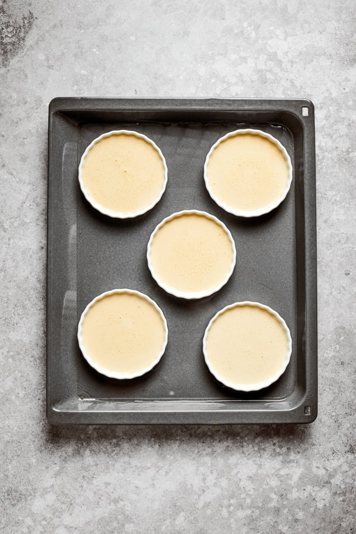 The silky custard in this Almond Vanilla Crème Brûlée lies beneath a glorious caramelized top. An elegant dessert that's surprisingly easy! Custard in ramekins set inside baking dish.