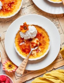 Almond Vanilla Crème Brûlée in ramekin set on plate with spoon.