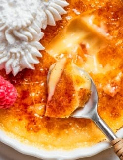 Spoon digging into Almond Vanilla Crème Brûlée with shattered caramelized sugar topping.