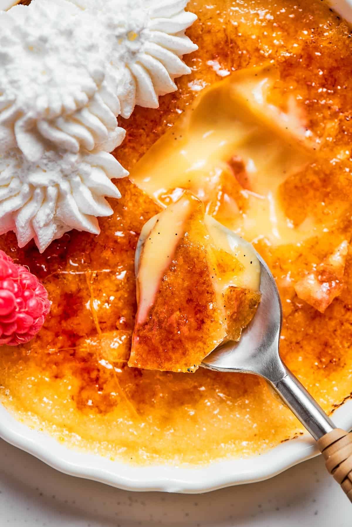 Spoon digging into Almond Vanilla Crème Brûlée with shattered caramelized sugar topping.
