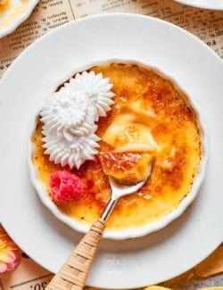 Almond Vanilla Crème Brûlée in ramekin with whipped cream and raspberry.