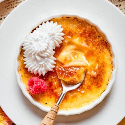 Almond Vanilla Cr&egrave;me Br&ucirc;l&eacute;e in ramekin with whipped cream and raspberry.