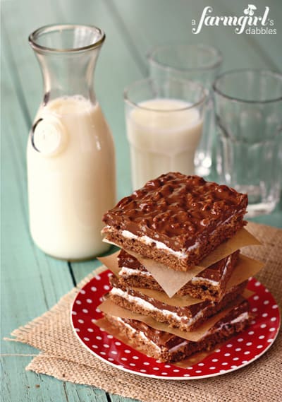 a stack of chocolate crispy bars and a pitcher of milk