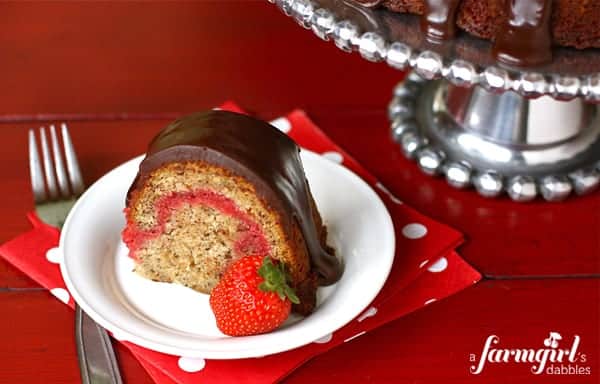 Slice of banana split bundt cake with chocolate frosting and a fresh strawberry on a round white plate