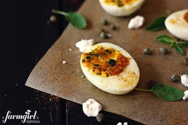 Mediterranean Deviled Eggs are stuffed with egg yolks, tangy feta, briny capers, and spicy cayenne. They're a fun twist on a classic recipe! Sautéed deviled eggs on parchment paper.