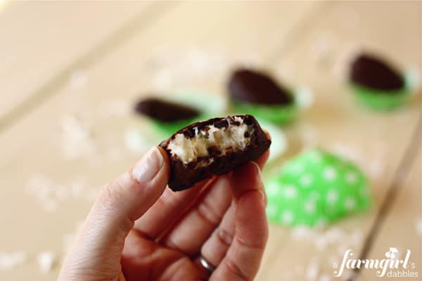 A hand holding a homemade chocolate dipped coconut cream egg with a bite missing