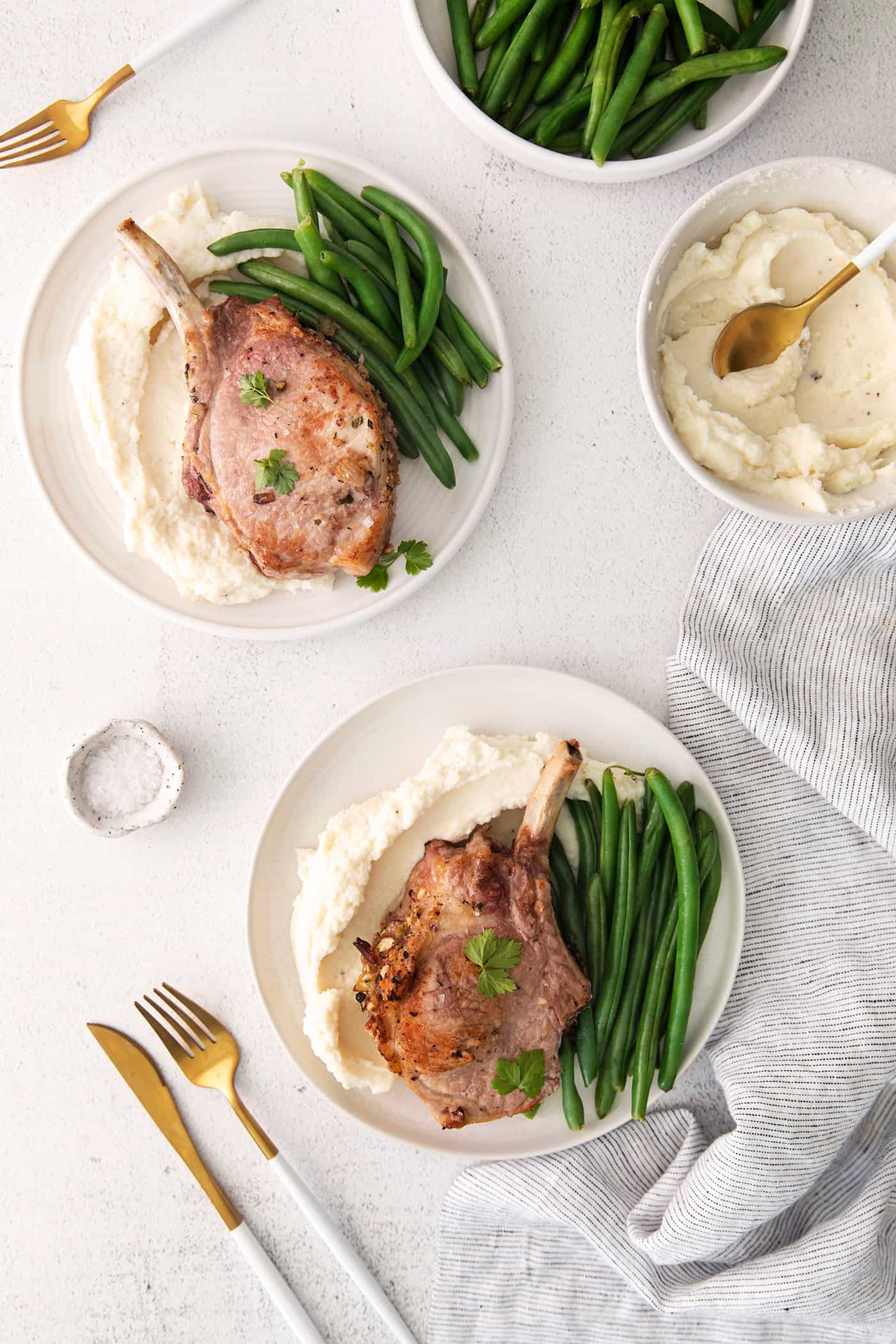 Overhead view of two plates with a stuffed pork chop, mashed potatoes, and green beans