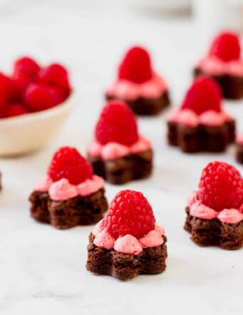 Several flower-shaped brownie bites topped with buttercream frosting and a raspberry