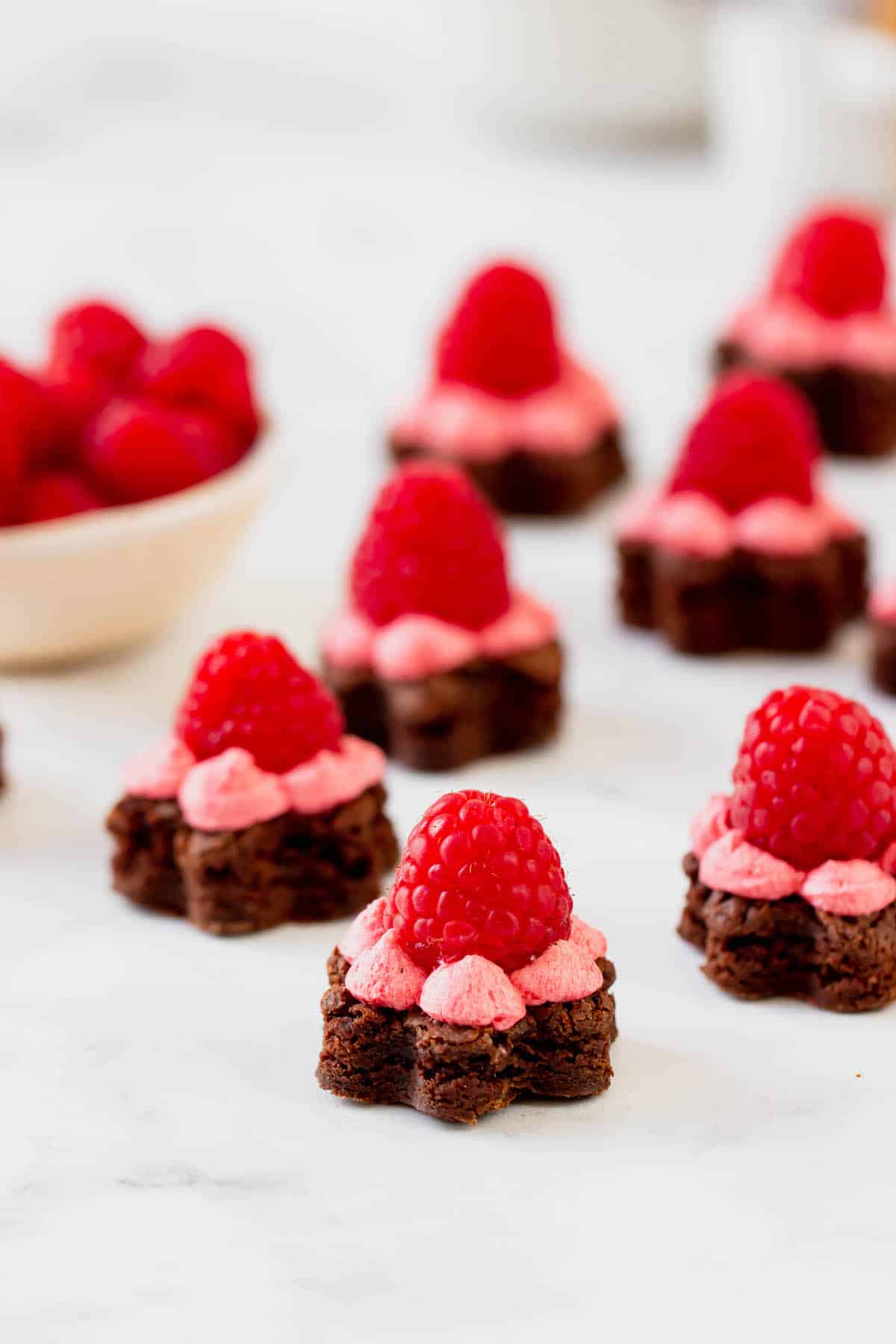 Several flower-shaped brownie bites topped with buttercream frosting and a raspberry