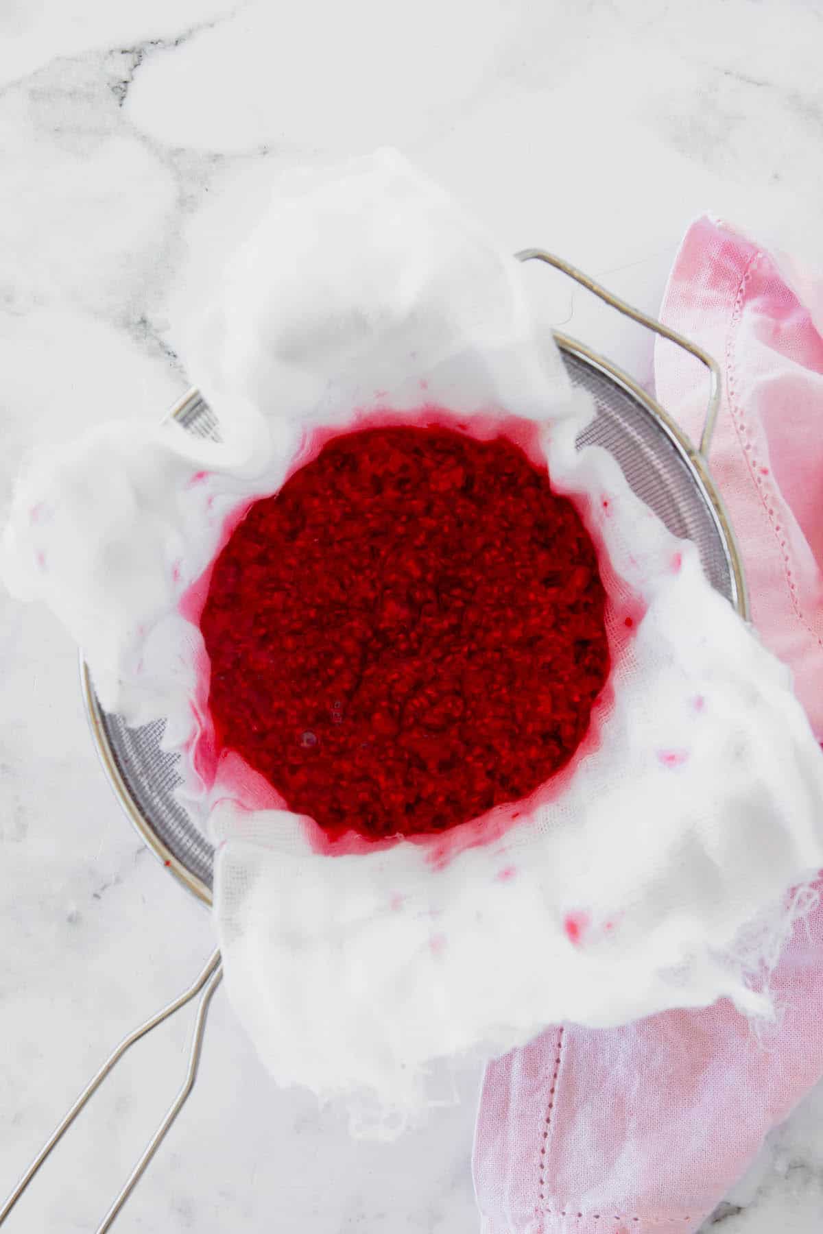 Raspberry sauce being strained in a cheese cloth