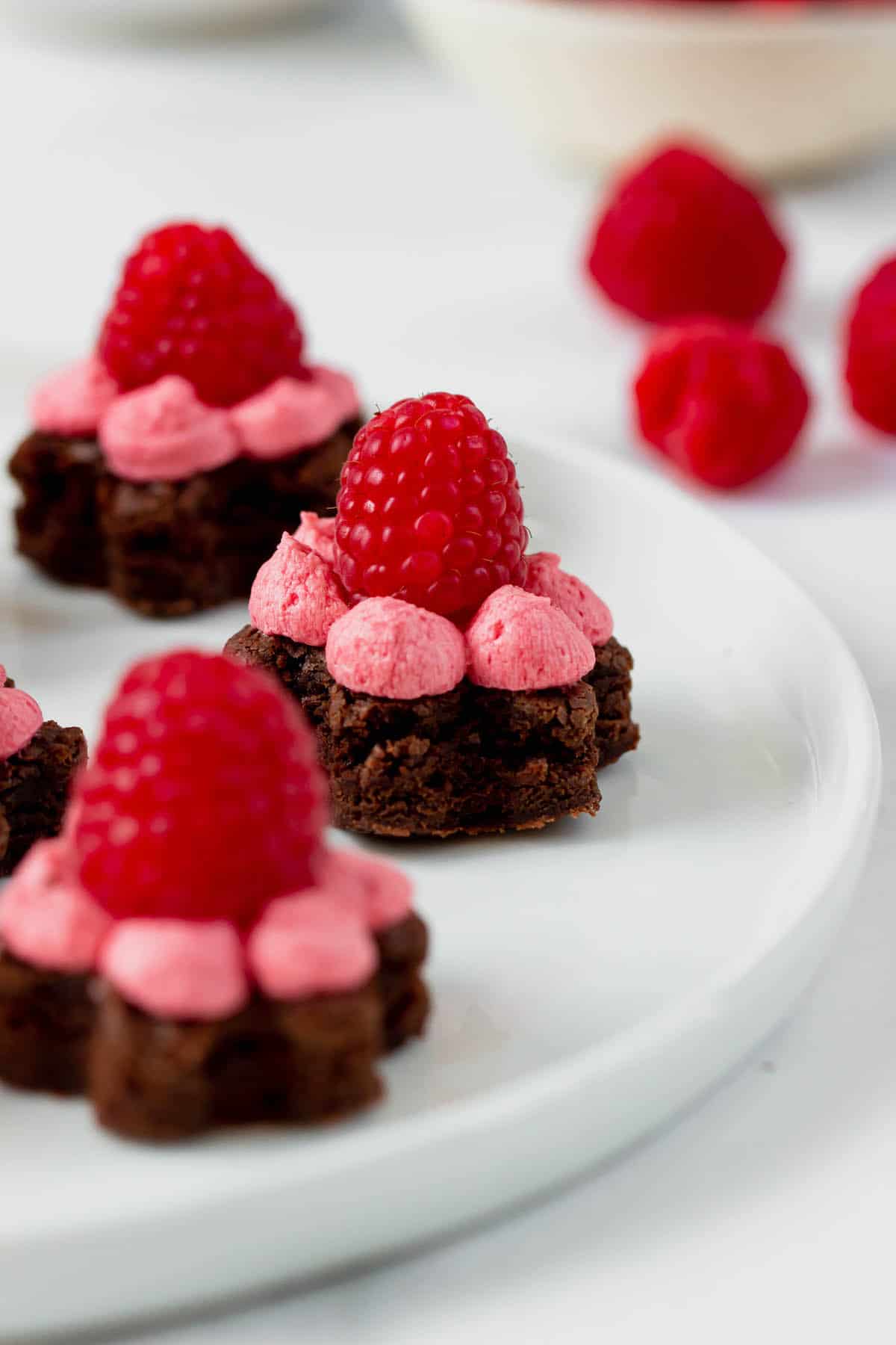 Close-up of 3 brownie bites topped with buttercream frosting and a raspberry