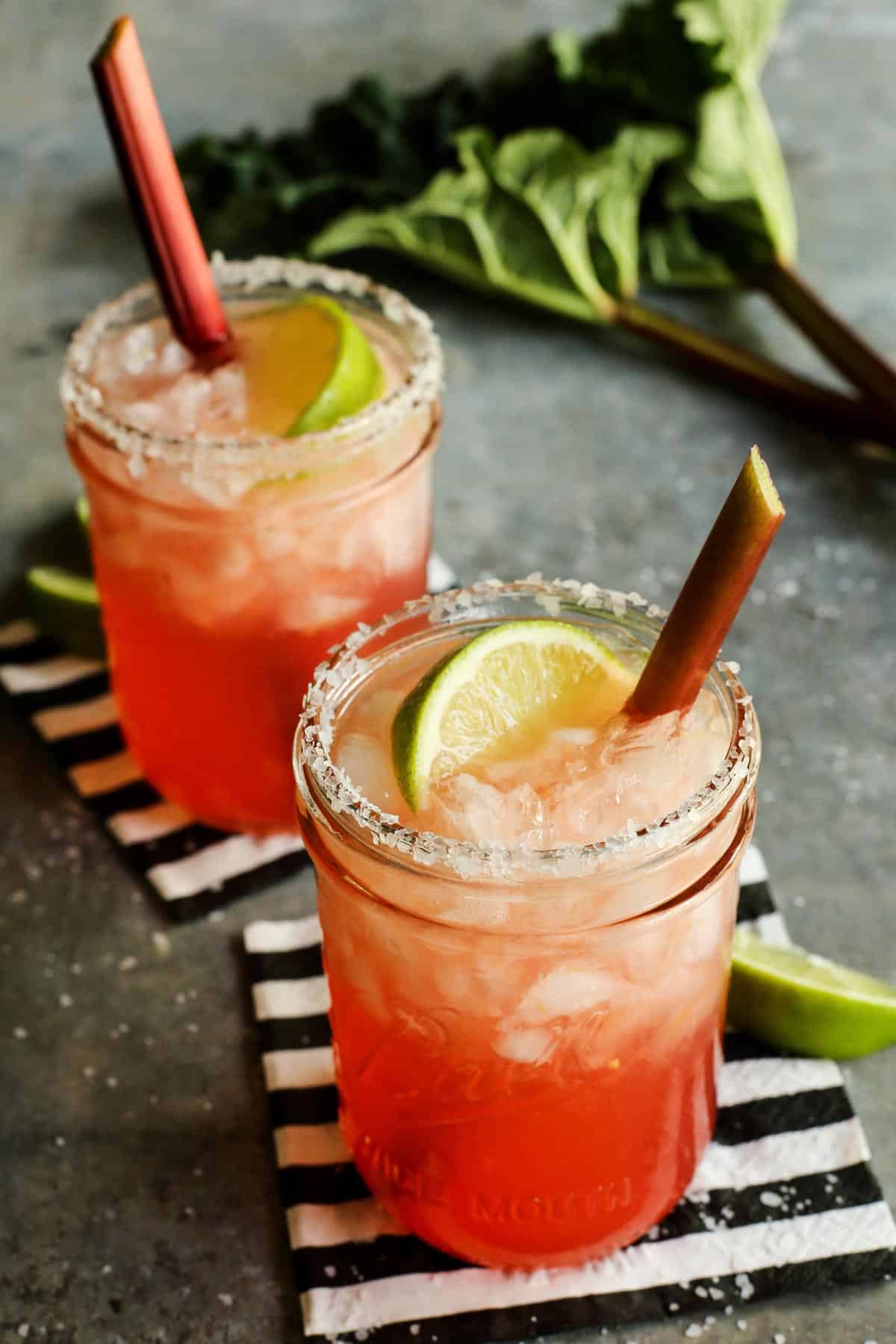 two mason jars of rhubarb margaritas plus fresh rhubarb