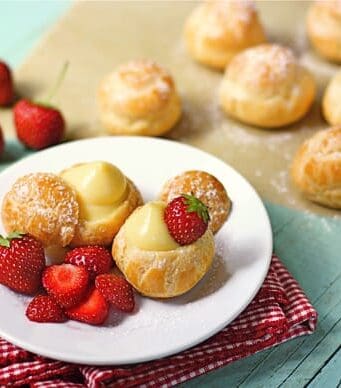 a plate with filled cream puffs and fresh strawberries