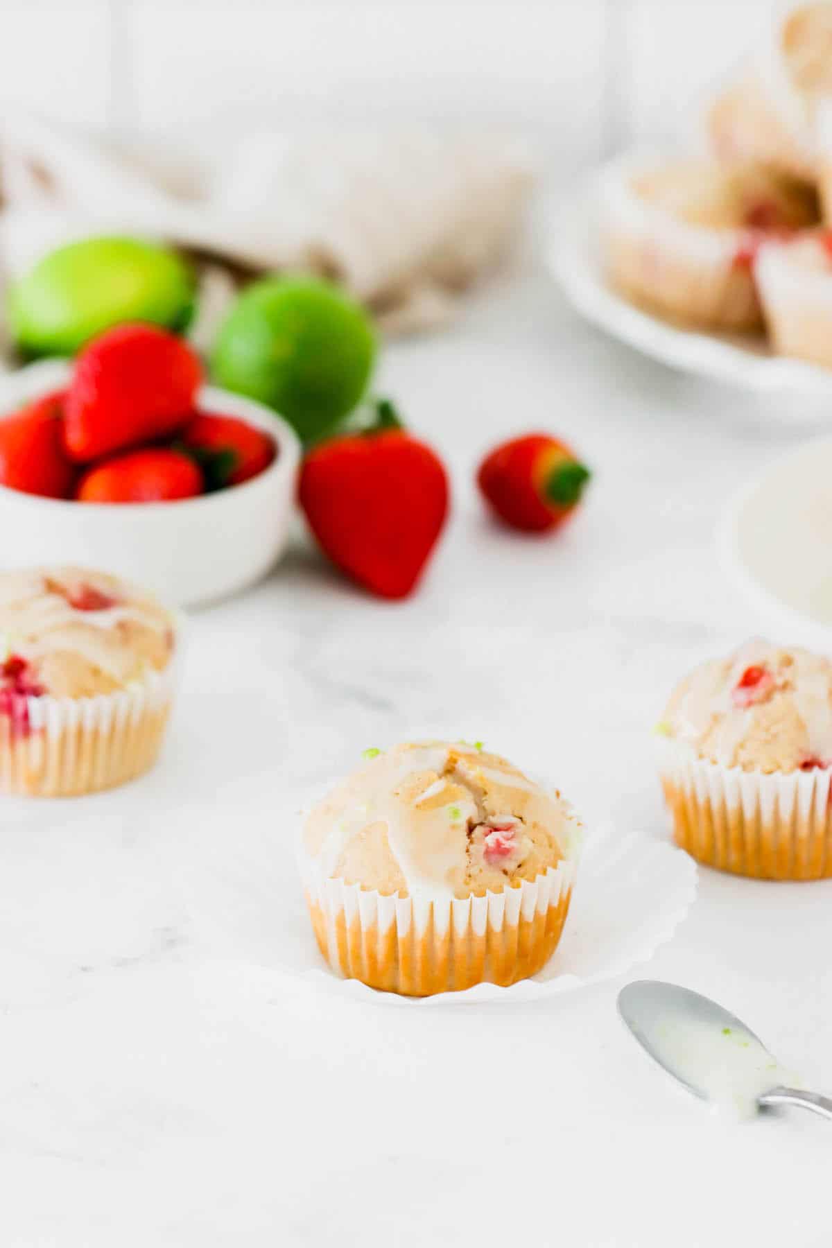 Three strawberry muffins with a bowl of strawberries in the background
