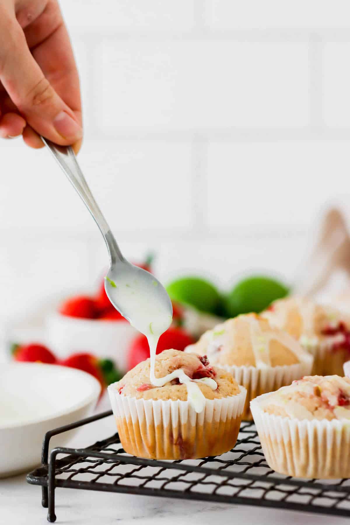 Lime glaze being drizzled over strawberry muffins