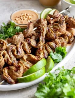 Coconut beef satay skewers on platter with peanut sauce, cilantro, and lime