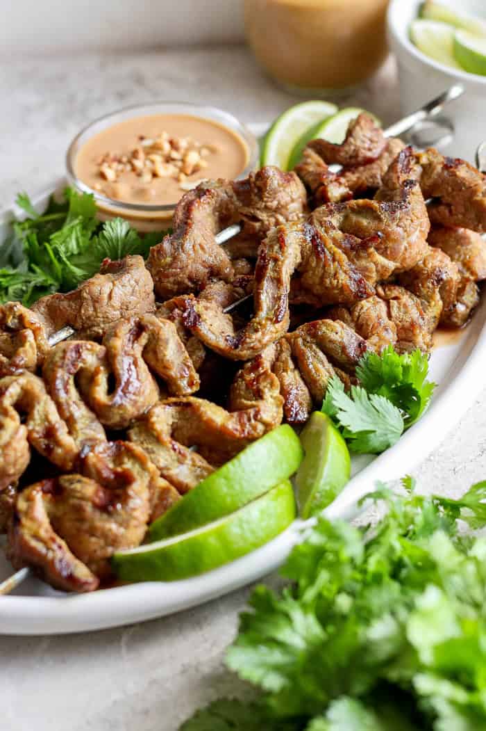 Coconut beef satay skewers on platter with peanut sauce, cilantro, and lime