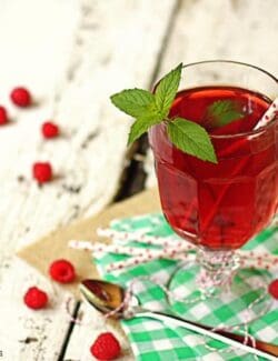 a glass cup of iced tea with fresh raspberries
