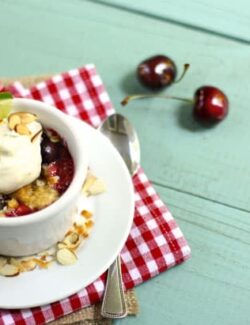 a white ramekin with cherry crumble and whipped cream