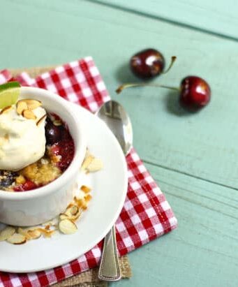 a white ramekin with cherry crumble and whipped cream