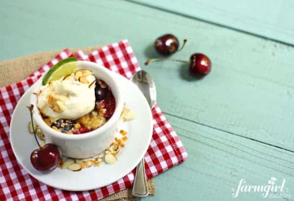 a white ramekin with cherry crumble and whipped cream