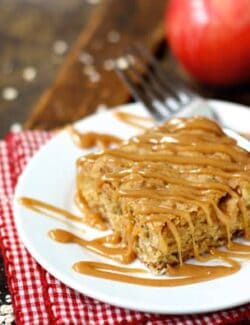 A Square Apple Oatmeal Bar on a Plate Beside Two Fresh Apples