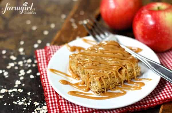 A Square Apple Oatmeal Bar on a Plate Beside Two Fresh Apples