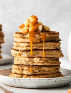 A stack of apple oat pancakes topped with diced apples and caramel syrup