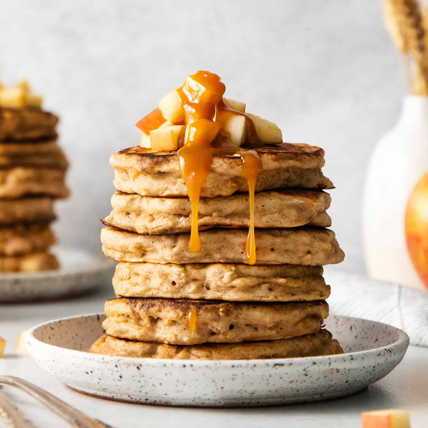 A stack of apple oat pancakes topped with diced apples and caramel syrup