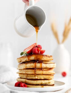 Syrup being poured over a stack of pancakes