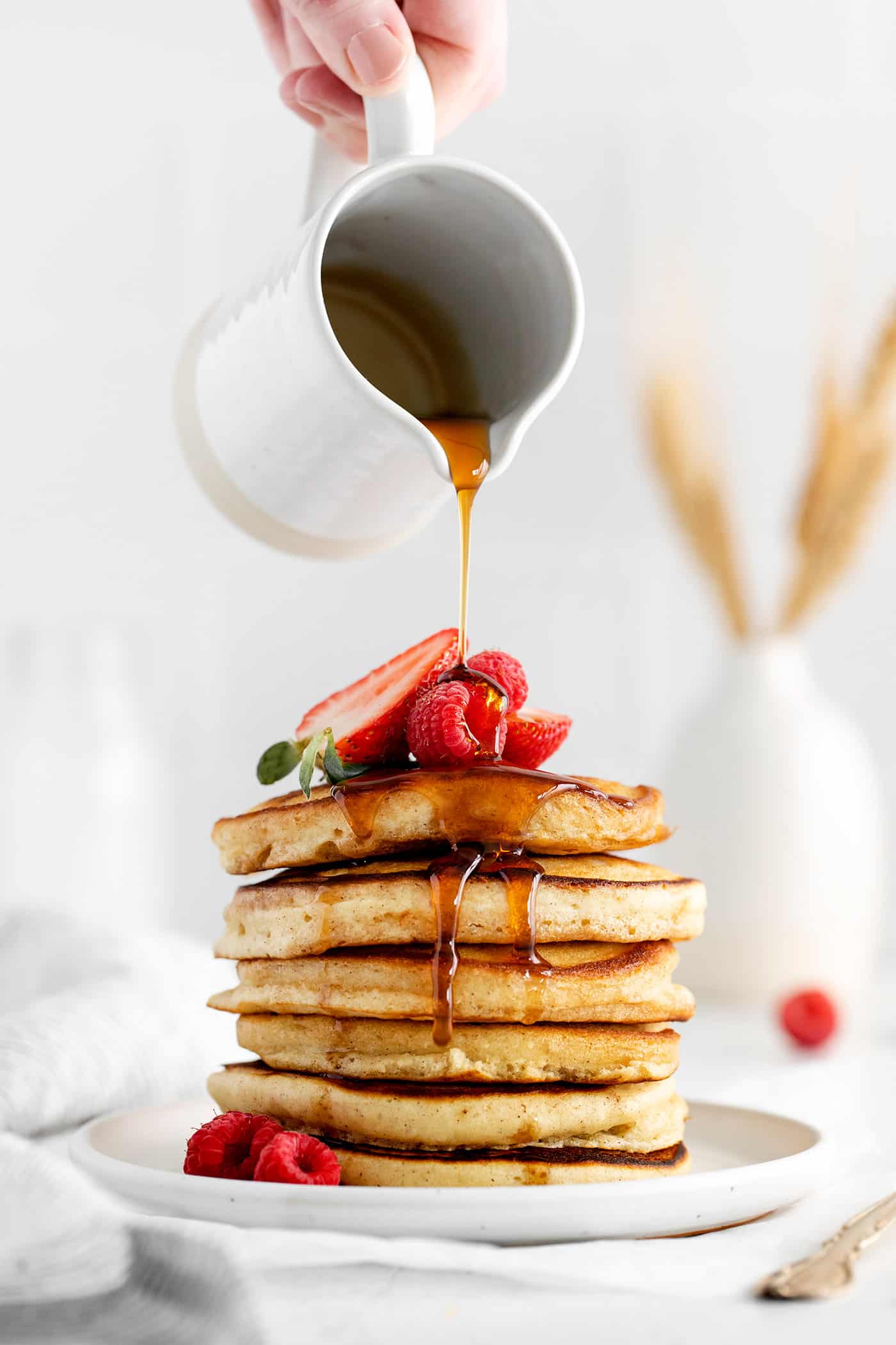 Syrup being poured over a stack of pancakes