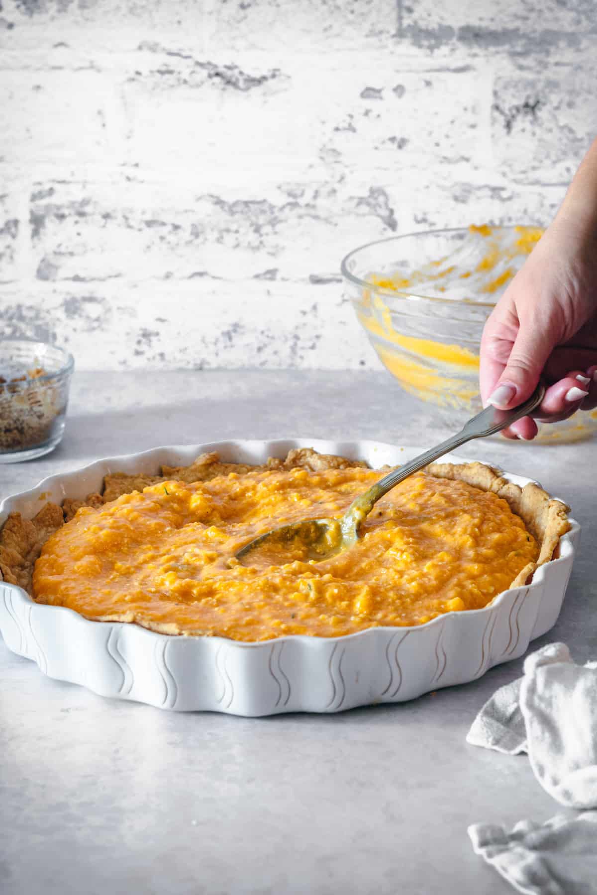 A spoon spreading roasted butternut squash in a tart pan